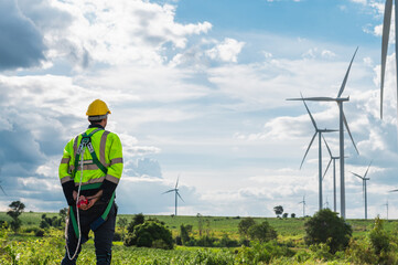  man in a yellow helmet stands in a field of wind turbines