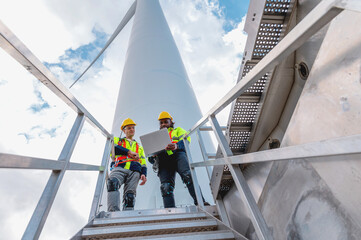 two men in safety gear are standing on a ladder next to a large wind turbine