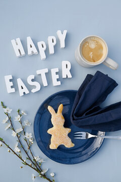 Happy Easter phrase, blackthorn twigs, mug of coffee and bunny shaped cake