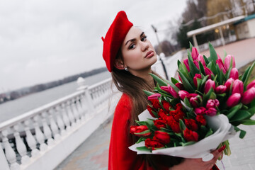 Young woman in red french beret standing on the pier near river cloudy weather in early spring...