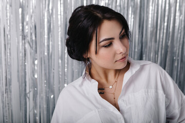 Beautiful pretty woman poses near silver foil glitter tinsel curtain. Shimmer fringe holiday...