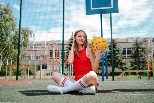 Basketball player sitting with ball on ground in schoolyard