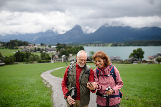 Active elderly couple hiking together in mountains, enjoying nature. Senior tourists looking at route on smartphone, online maps.