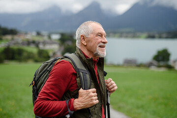 Portrait of smiling elderly man walking outdoors with trekking poles, going on hiking trail. Senior...