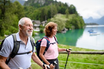 Portrait of active elderly couple hiking together in mountains. Senior tourists walking with trekking poles. - obrazy, fototapety, plakaty