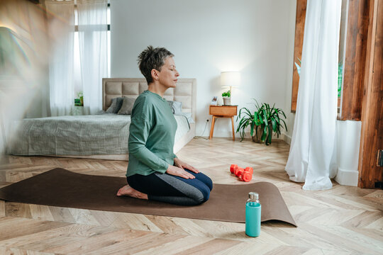 Woman practicing Vajrasana sitting on exercise mat at home