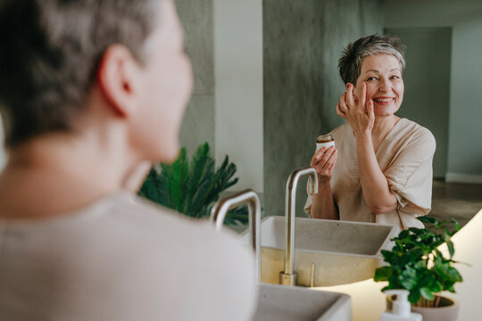 Smiling woman doing skincare looking in mirror at home