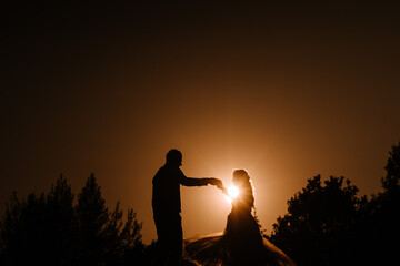 Valmiera, Latvia - August 13, 2023 -  a bride and groom are silhouetted against a dramatic orange...