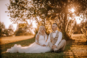 Valmiera, Latvia - Augist 13, 2023 - A bride and groom seated on the grass, with the sun filtering...