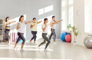 Group of women doing fitness and self defense workout to stay in good shape and be able to defend themselves. Happy sporty powerful ladies exercising at gym, clenching fists, learning fighting moves