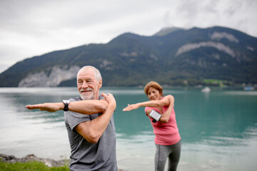 Senior couple doing outdoor yoga, tai chi, pilates by the lake in the autumn. Elderly husband and...