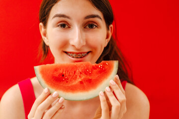 A close-up of a female teenager mouth with dental braces and a piece of delicious watermelon. The...