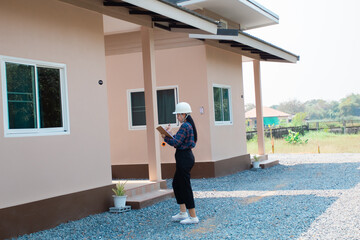 Asian house's construction inspector female in hard hat reviews architectural plans examining...