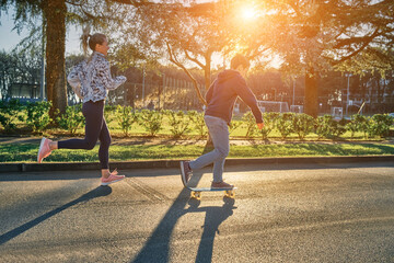 Happy family outdoors, mother and son go in sports, Boy rides skateboard, mom runs on sunny day. Silhouette people at sunset. Health care, authenticity, sense of balance and calmness. - obrazy, fototapety, plakaty