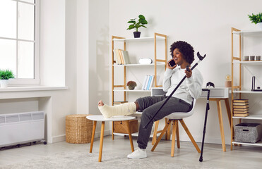Handicapped young african american woman sitting at home on chair in rehabilitation with crutches...