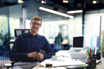 Handsome male architect looking at camera and smiling while sitting in the office. - 779506728