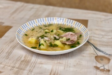 Bowl of traditional chicken soup served in a white plate on background tablecloth. Close-up