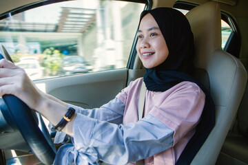 Happy asian indonesian muslim woman driving car wearing hijab and casual outfit
