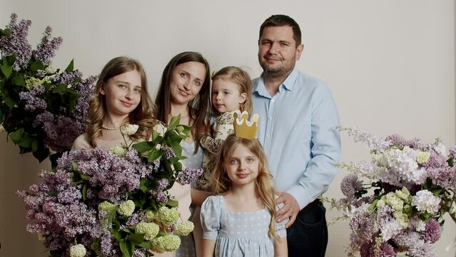 Family portrait standing for photo inside on a white background with flowers in the studio. Portrait of happy family in slow motion. Happy young family together with children.