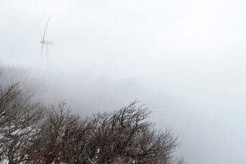 View of the wind turbine in the fog and snow on the winter mountain