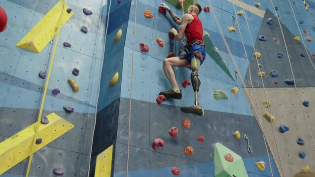 Low angle view of man with prothetic leg climbing wall in indoor gym as his partner holding rope