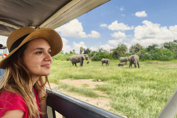 A Caucasian girl in a hat looks at animals in the savannah. The concept of travel and adventure in the wild. Young woman discover african nature by car with an open roof. Tanzania safari