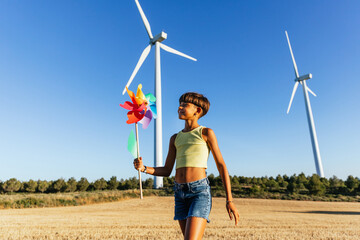 Smiling girl playing with a colorful pinwheel in the sunlight.
