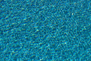 Water background. Blue water, ripples and highlights. Texture of water surface and tiled bottom.