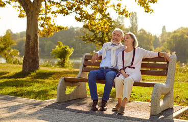 Seniors rest outdoors. Beautiful stylish elderly couple in love is sitting on bench in city park on warm summer evening. Mature Caucasian family on walk. Concept of long and happy love and marriage.  - Powered by Adobe