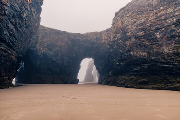 Playa de Las Catedrales in foggy day. Catedrais beach in Ribadeo, Lugo, Galicia, Spain. Natural archs of Cathedrals beach. Mystical landscape. Moody rock formations on misty day. Travel destination - 779531382