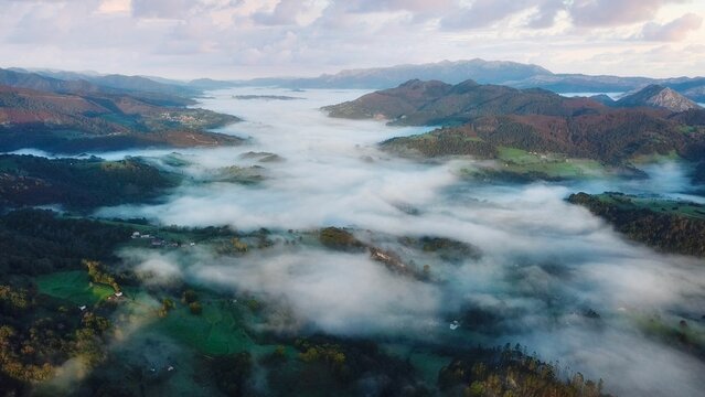 Aerial shot of a fog layer covering the vegetation and the hills of a beautiful landscape