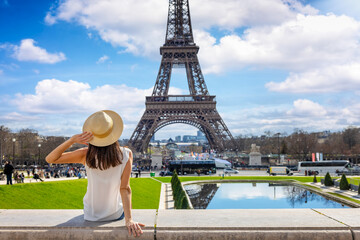 A tourist woman enjoys the beautiful view of the Eiffel Tower in Paris, France, during a sunny spring day - obrazy, fototapety, plakaty