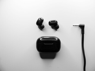 Top view grayscale of wireless earbuds with a black powerbank and a wire of another device