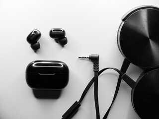 Flat lay grayscale of wireless earbuds and a headset with a wire on an isolated background