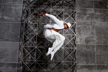Energetic African American male dancer jumps and twirls in a studio wearing white attire, executing...