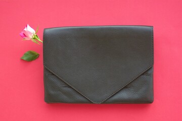 elegant black leather clutch with bright pink rose bud and separated green leaf on a background of pink paper
