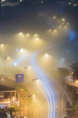 Naklejka premium Long exposure shot of traffic lights and illuminated street lanterns on a foggy night