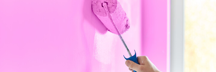Male hand painting wall with paint roller. Painting apartment, renovating with lavender color paint