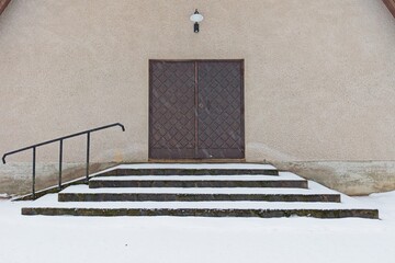 Old weatherd wooden door on a stone building with stairs and handrail in winter with snow on the...