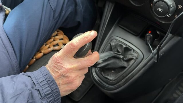 Close-up of an old wrinkled-skinned man's hand shifting gears on the lever of a car's manual transmission