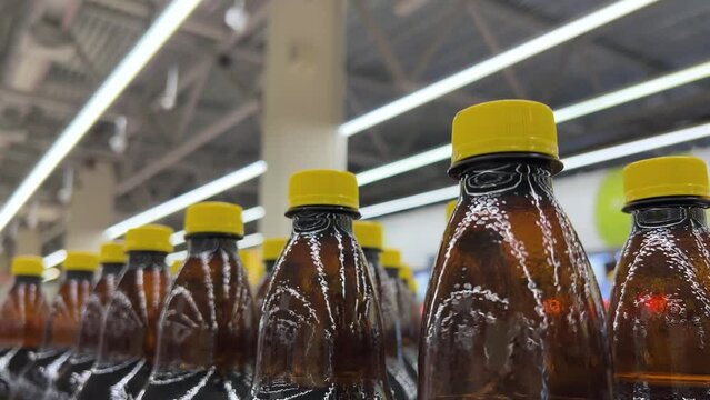 Many brown plastic bottles of drinks with yellow caps on store shelf in supermarket, warehouse