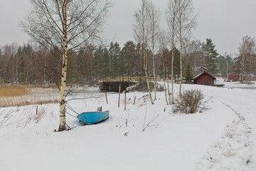 Winter landscape view with wooden bridge over sea strait, leafless trees, boat dragged ashore and...