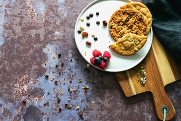 Top view of cookies with berries in white plate on wooden board
