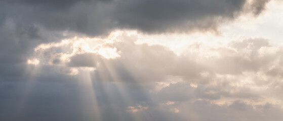 Sunbeams piercing through brooding clouds, creating a dramatic and hopeful skyscape