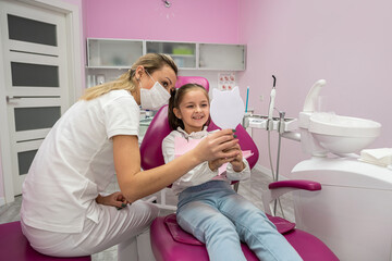 little female patient in the dental chair looks at her teeth after their treatment.
