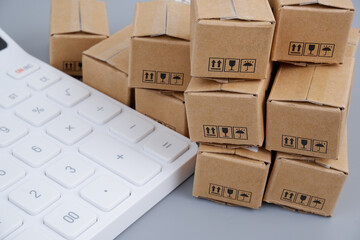 Cost of goods, taxes and shipment concept. Close up of many carton boxes and calculator.	