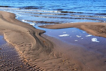 Closeup shot of a sandy shore in front of a wavy blue sea on a sunny day