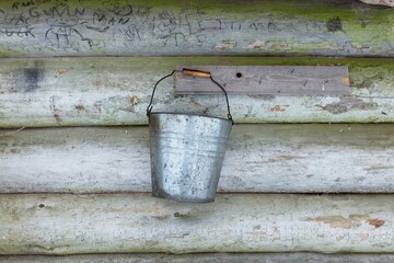 Old retro bucket hanging on wooden shelter wall. 