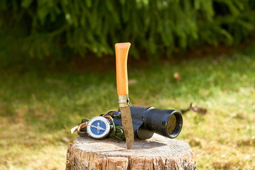 A rustic knife with a wooden handle, a vintage monocular, and a handheld compass rest on a wooden...