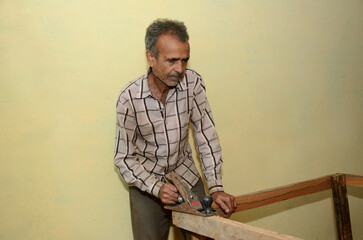 Indian old man working in a wood workshop with a plane